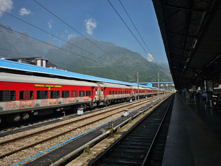 A vibrant red train at an outdoor station with scenic mountain backdrop, ideal for travel themes.