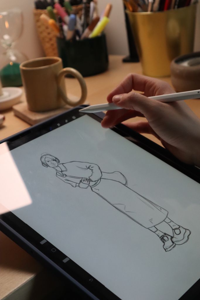 A person uses a stylus to draw on a tablet in a cozy workspace setting.