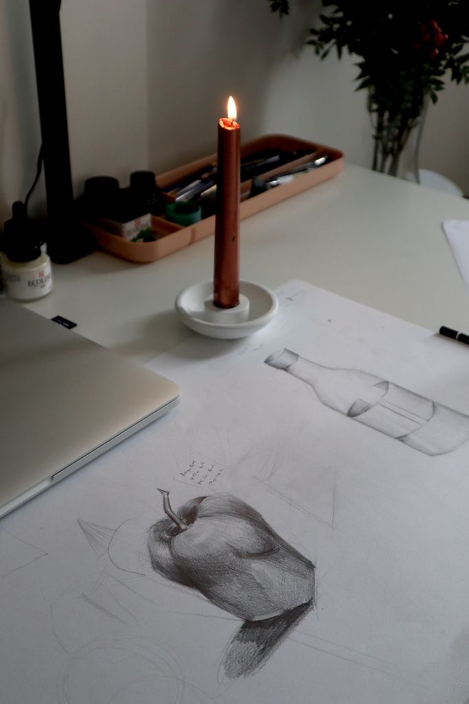 Cozy artist's desk with candle light illuminating sketches and art supplies.