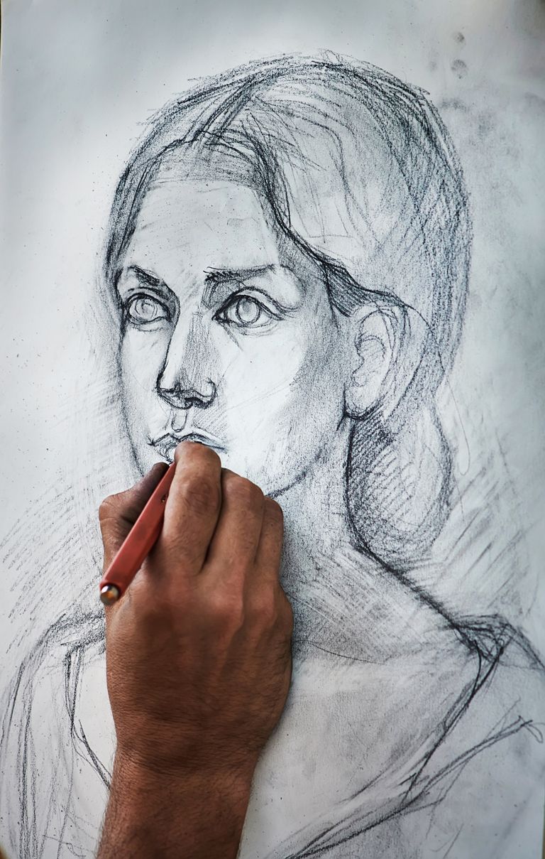 Crop unrecognizable person drawing portrait of charming woman with pencil on canvas in art studio