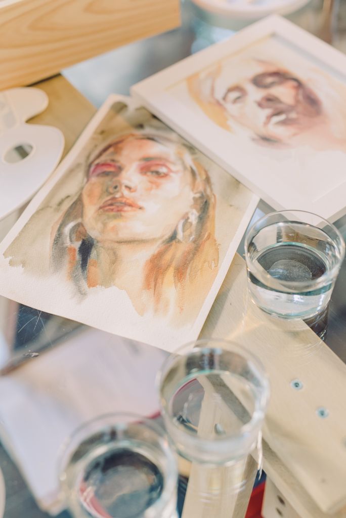 A collection of artistic watercolor portraits showcasing vibrant creativity on a glass table.