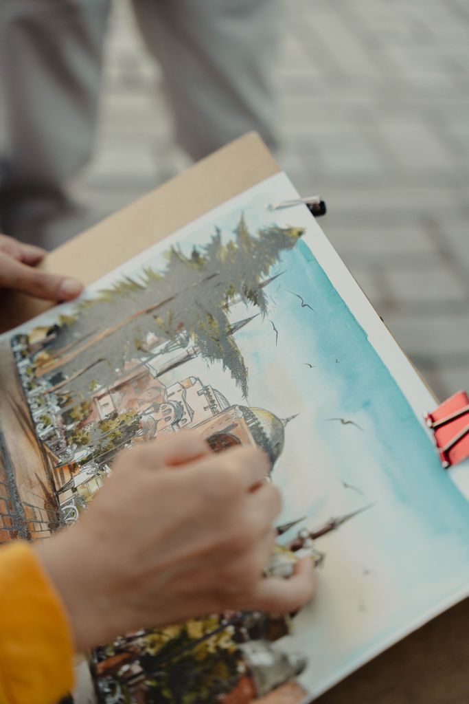 Close-up of an artist sketching a cityscape with watercolor paints outdoors.
